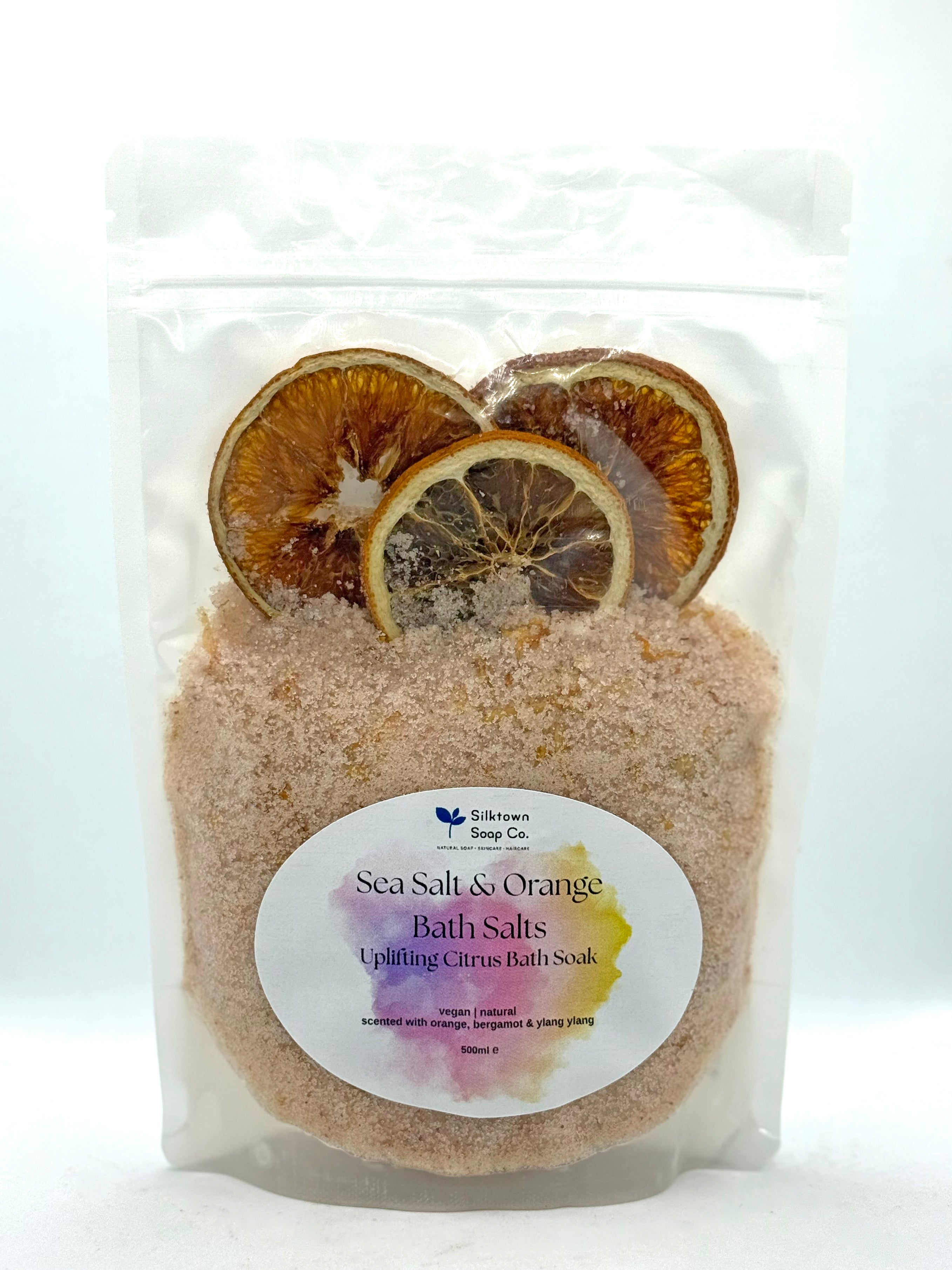 Packaged sea salt and orange bath salts with dried lemon slices on a white background
