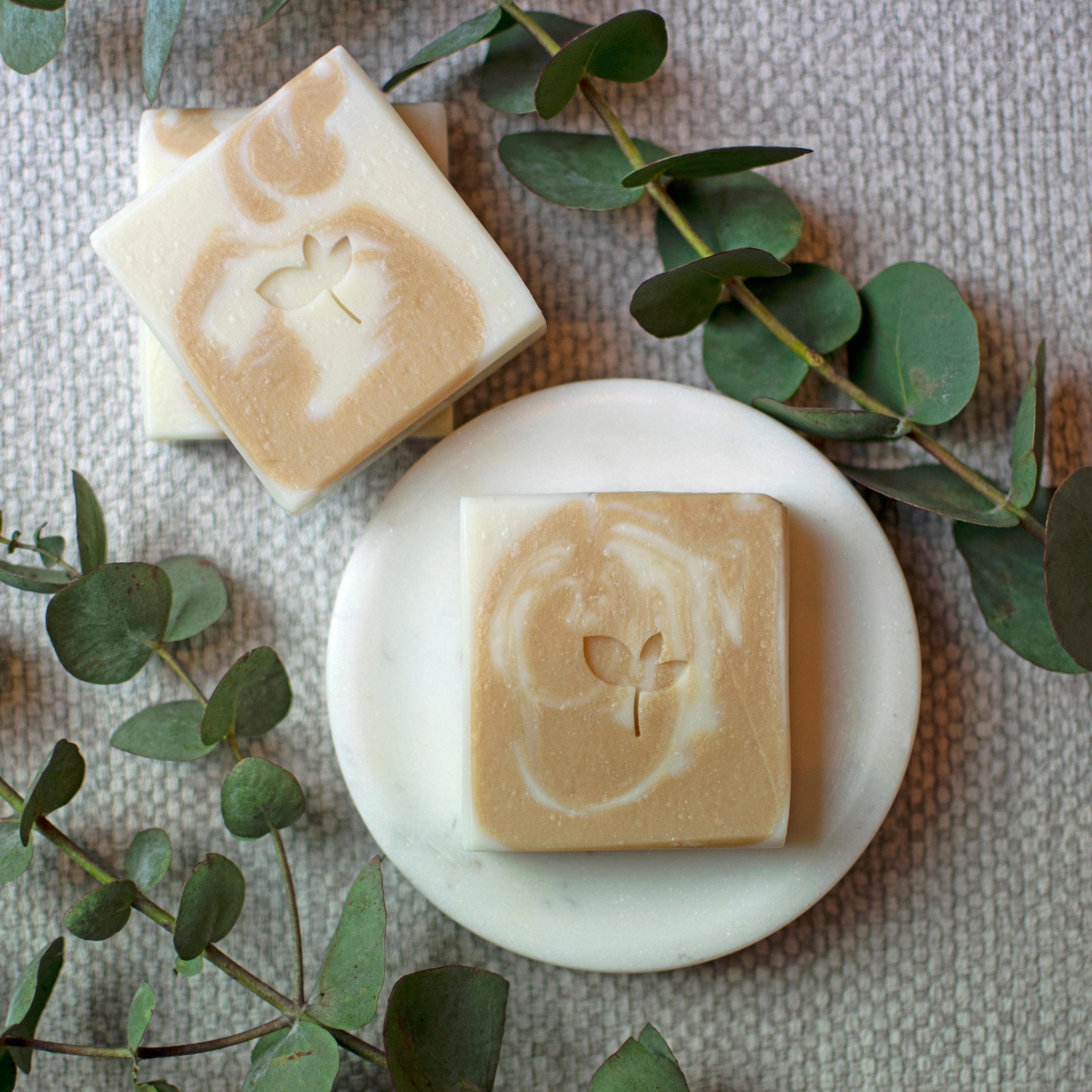 Two Buttermint natural soap bars with eucalyptus leaves and a round soap dish