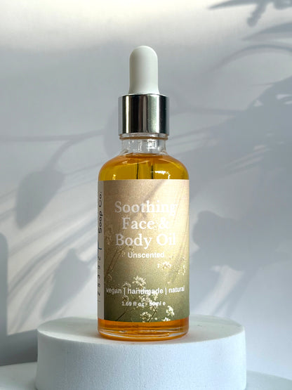Bottle of Soothing Face &amp; Body Oil on a white pedestal with a light gray background