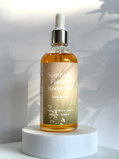 Bottle of Soothing Face &amp; Body Oil on a white pedestal with a white background