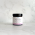 A small amber glass jar of Silktown Soap Co. Soothing Skin Cream with a black lid and a white label featuring a pink band, set on a light marble surface with a matching marble background.