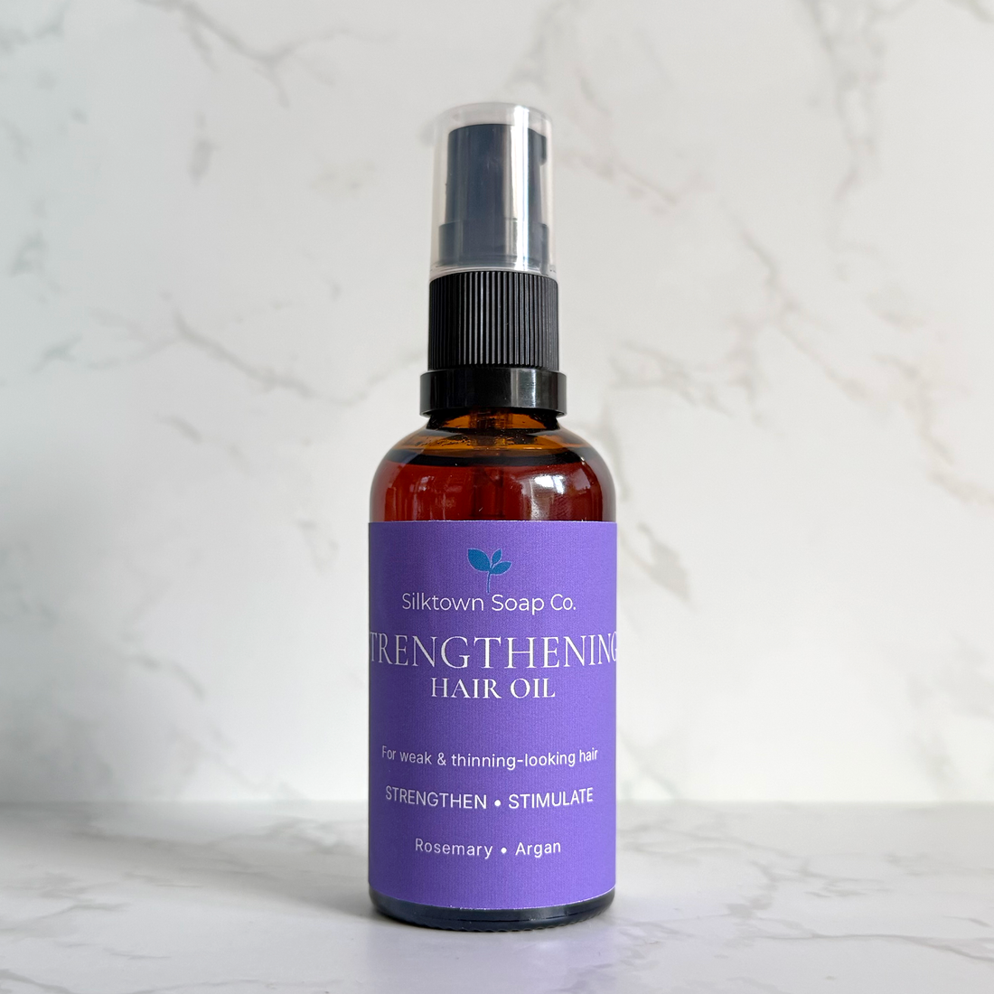 Silktown Soap Co. Strengthening Hair Oil in an amber glass spray bottle with a purple label, set against a white marble background.