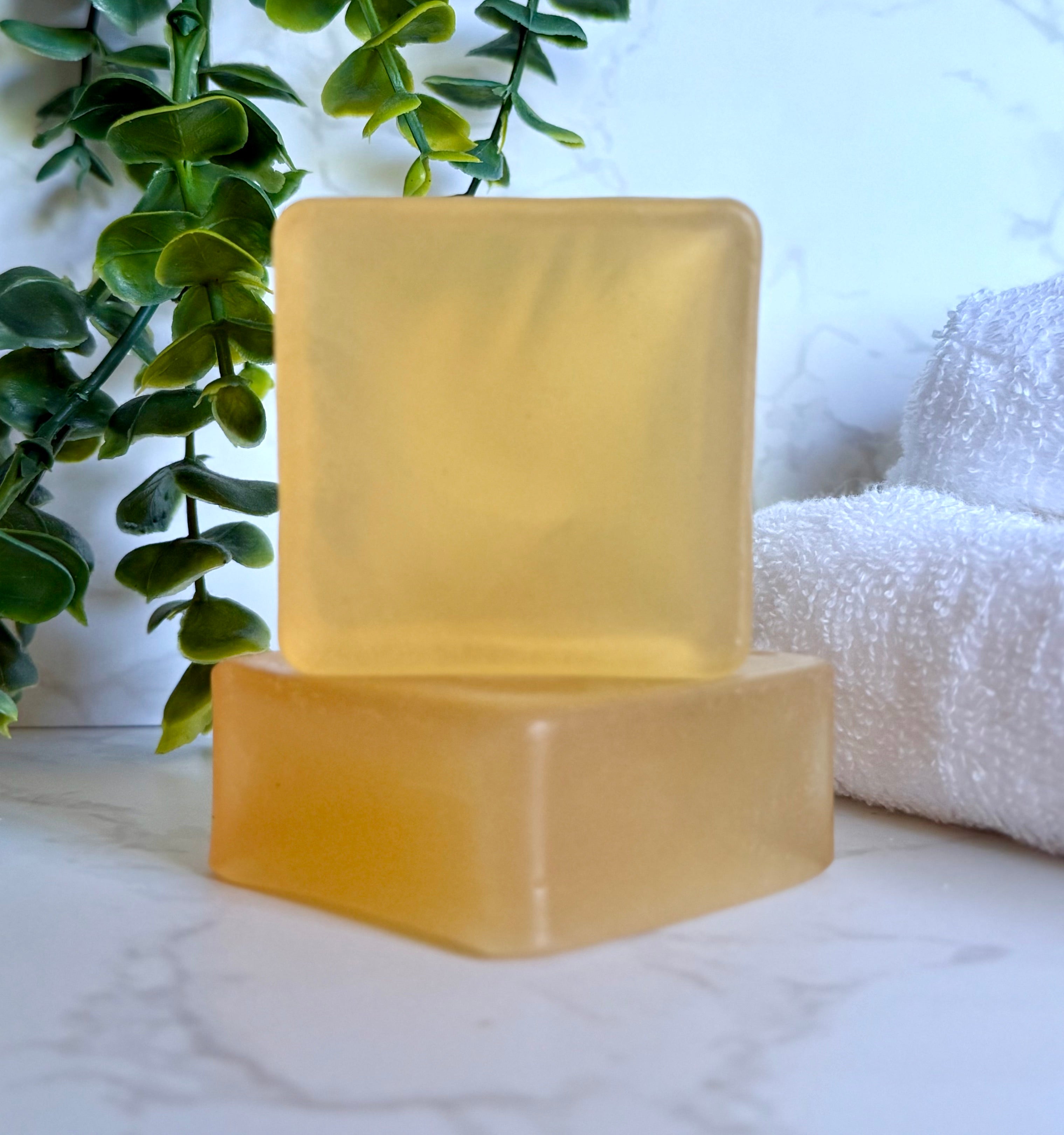Two yellow soap bars on a marble surface with greenery and a towel in the background.