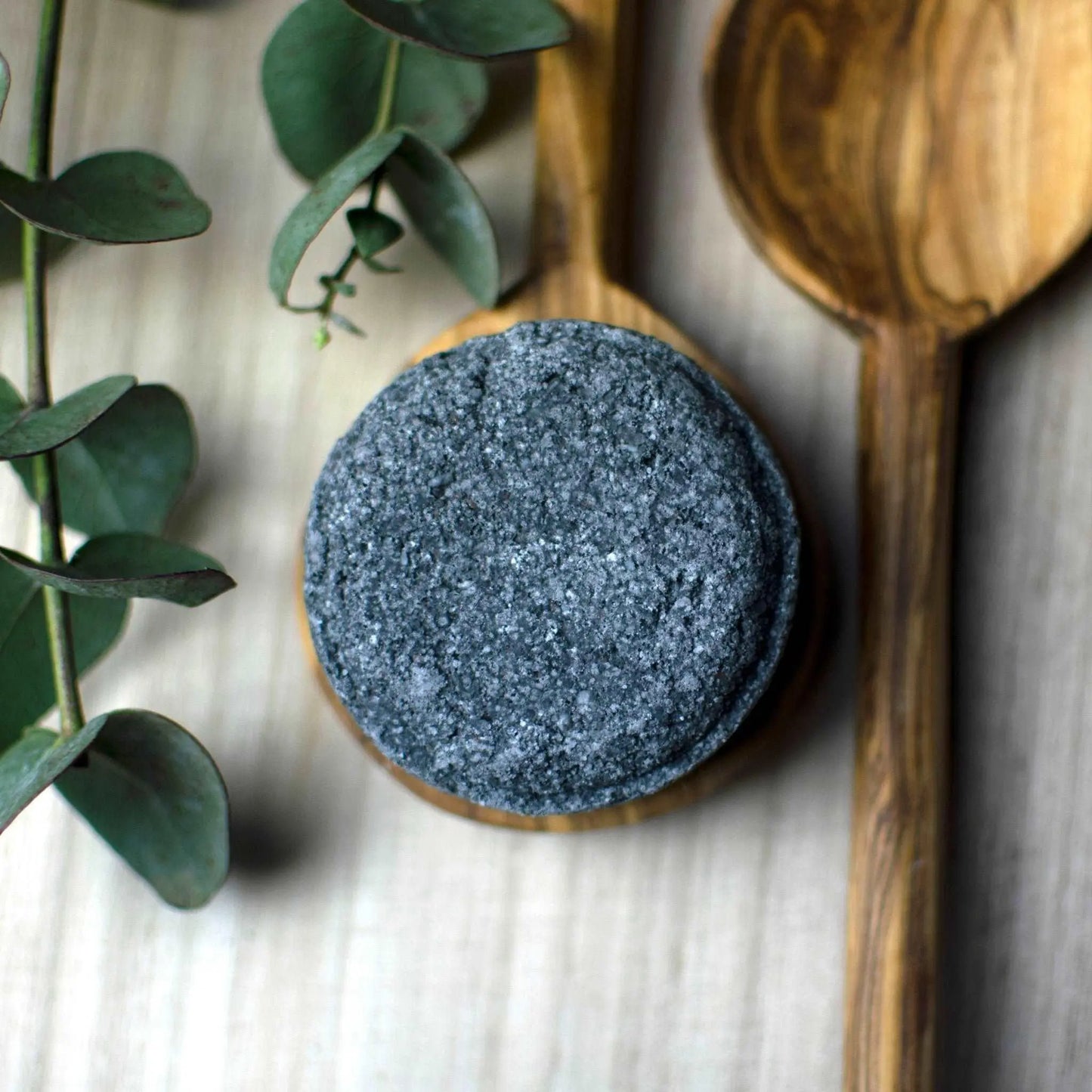 A Walk in the Clouds luxury bath salt soak bomb on a wooden spoon surrounded by eucalyptus