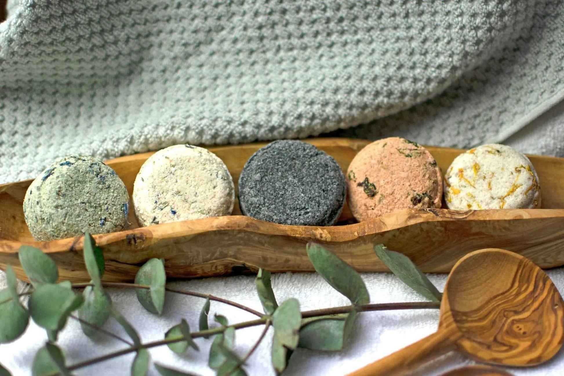 five Natural vegan bath soaks in a wooden dish with towels and botanicals