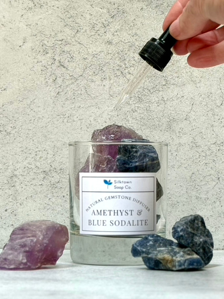 Amethyst and blue sodalite natural gemstone diffuser with a hand using an essential oil over it on a neutral background