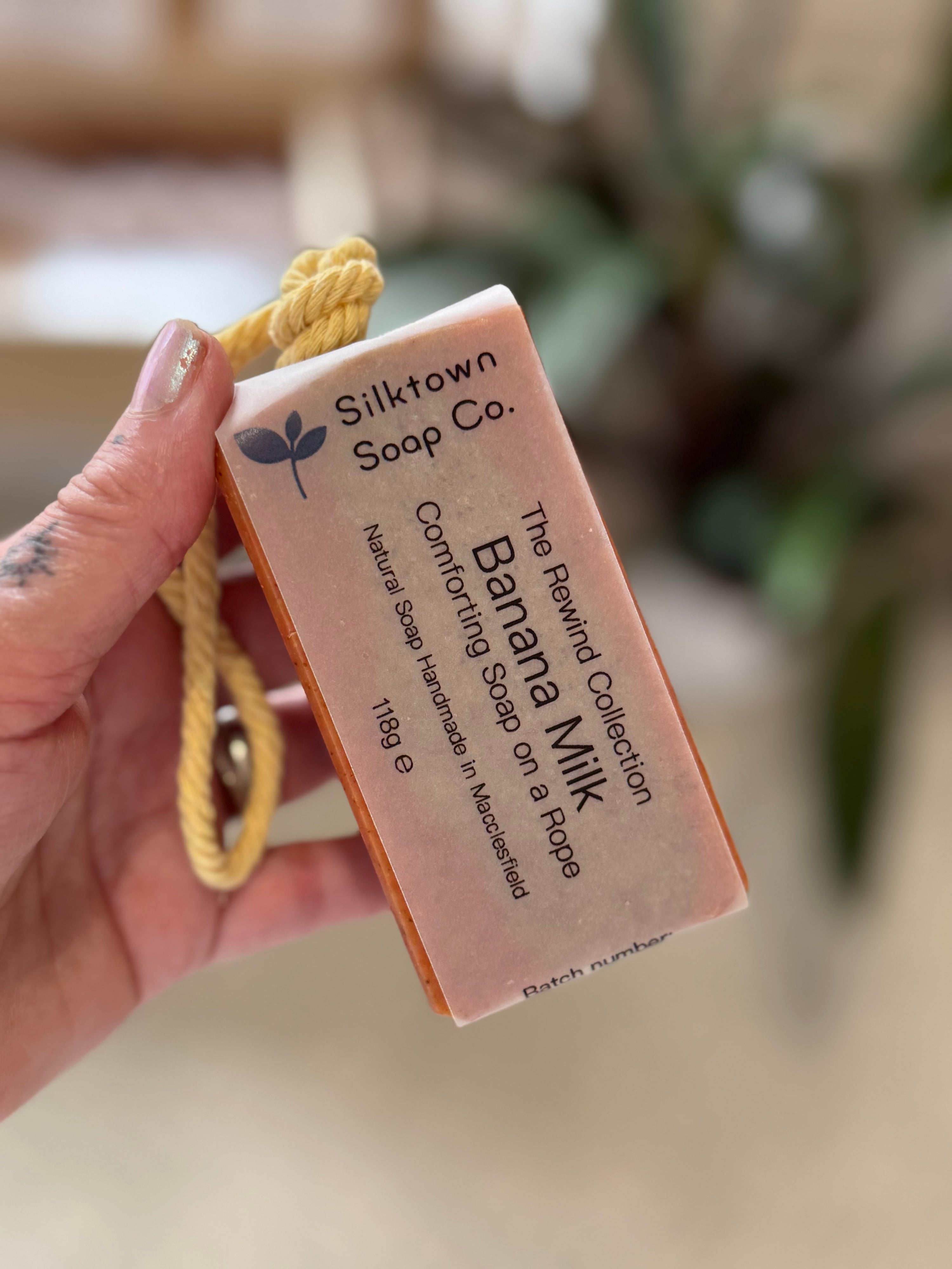 banana milk natural soap on a rope held up in the air with a blurred background
