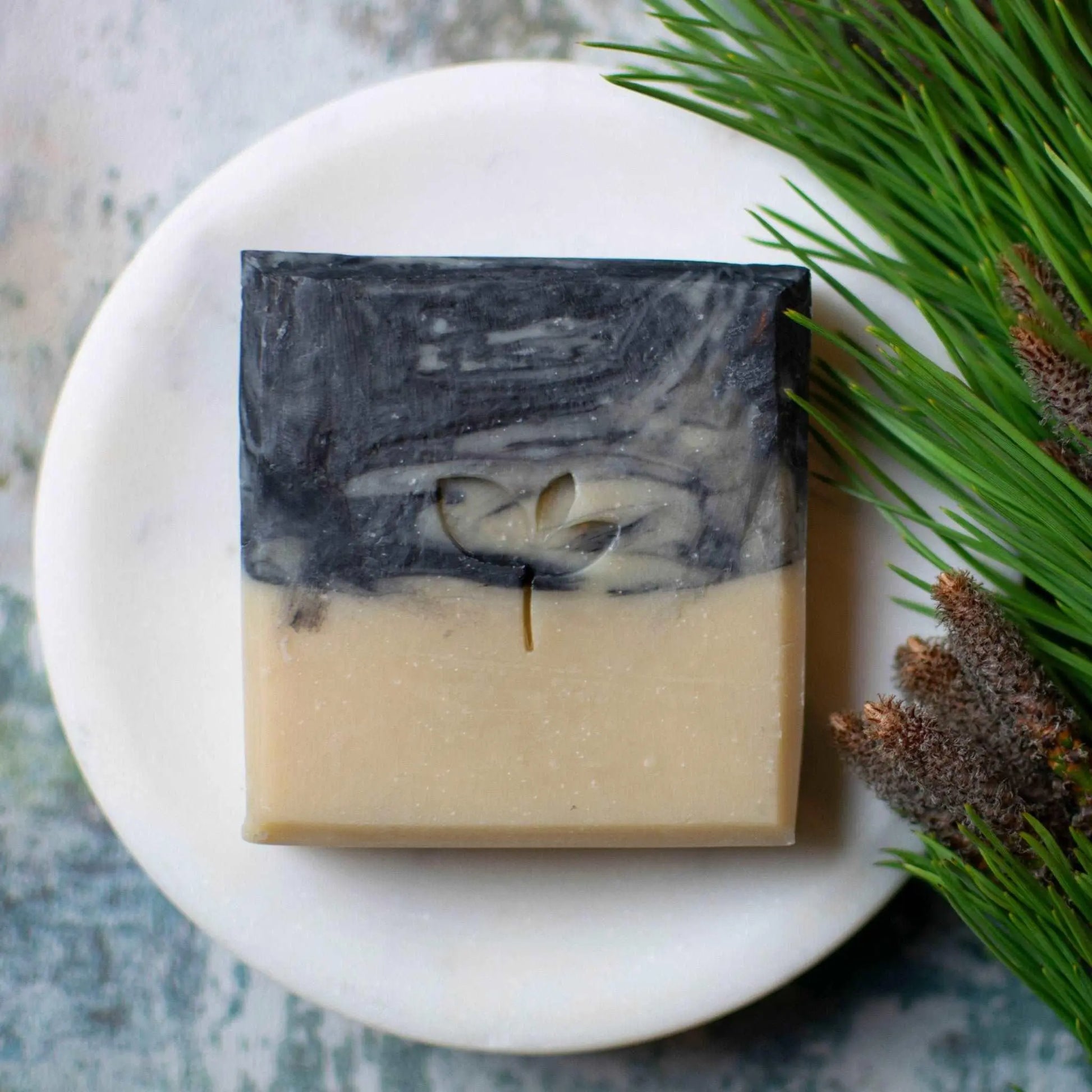 a bar of Cedarwood and Stout natural soap on a dish next to some botanicals