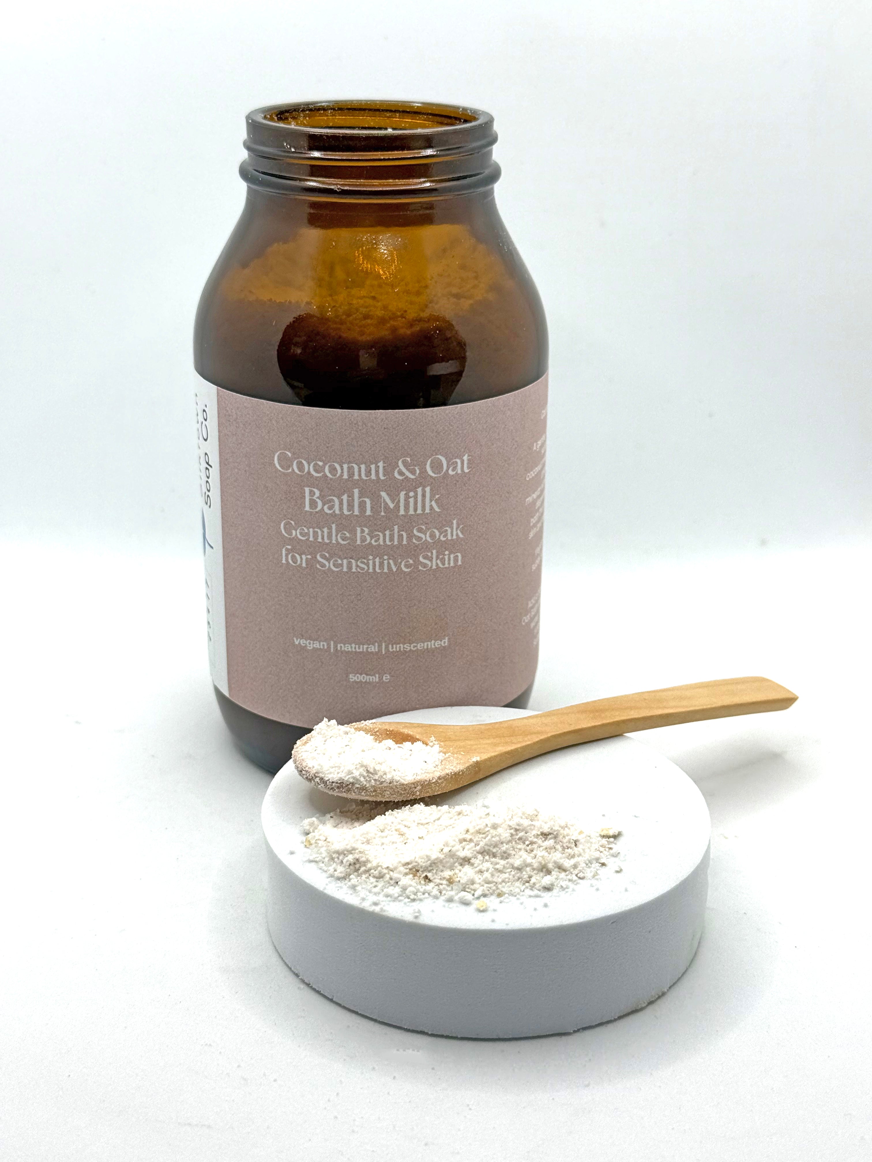 Coconut &amp; Oat Bath Milk with a wooden spoon and container on a white background