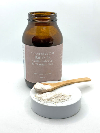 Coconut &amp; Oat Bath Milk with a wooden spoon and container on a white background