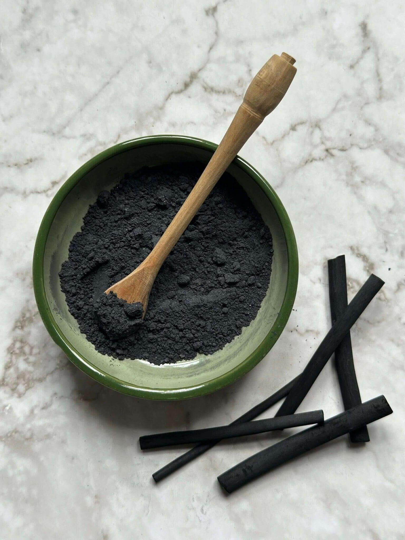 Detox Natural Clay Mask in a bowl with a wooden spoon and some natural charcoal sticks before being mixed 