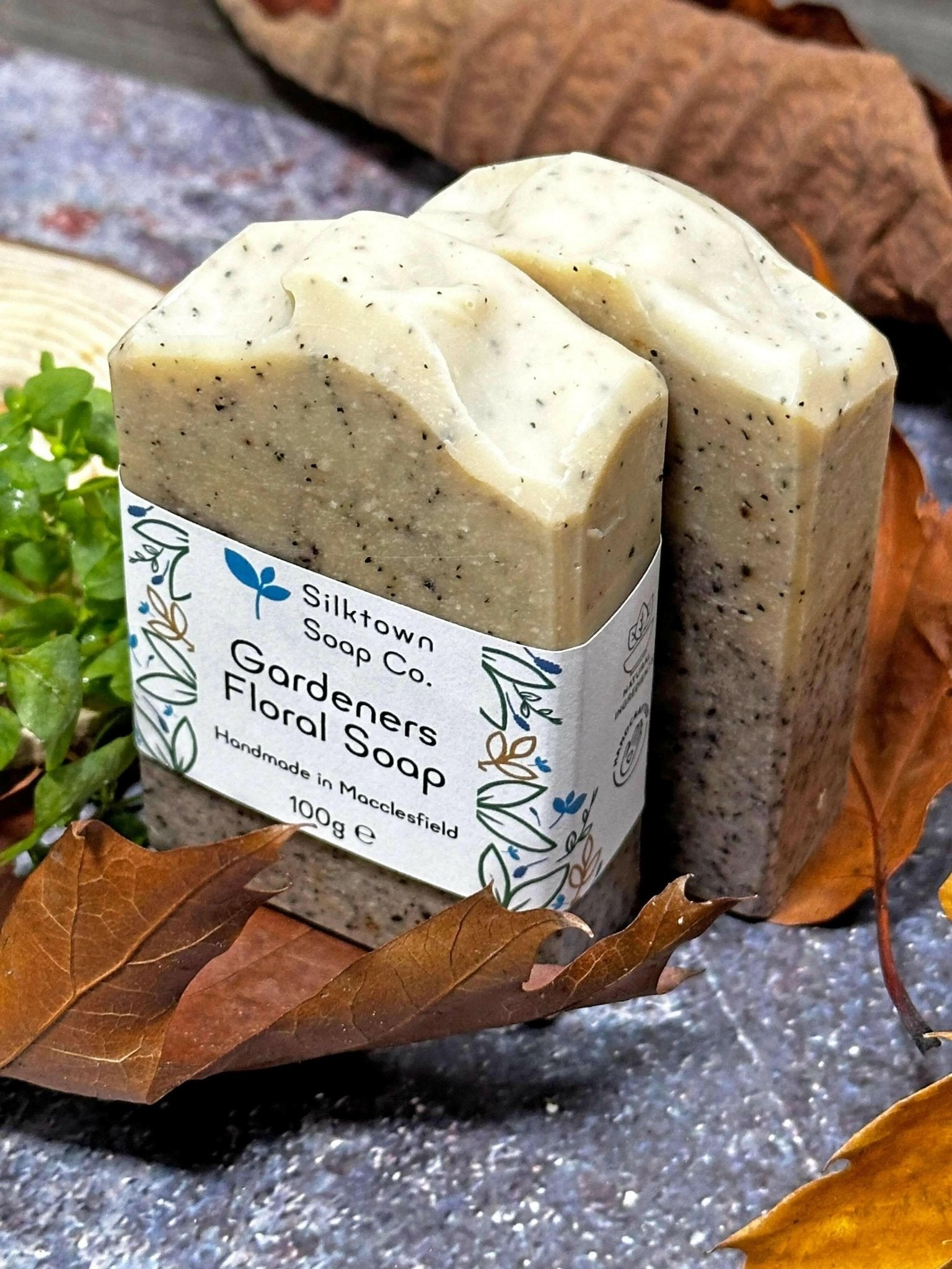 gardeners floral handmade natural soap bar with label amongst leave foliage, wood and stone