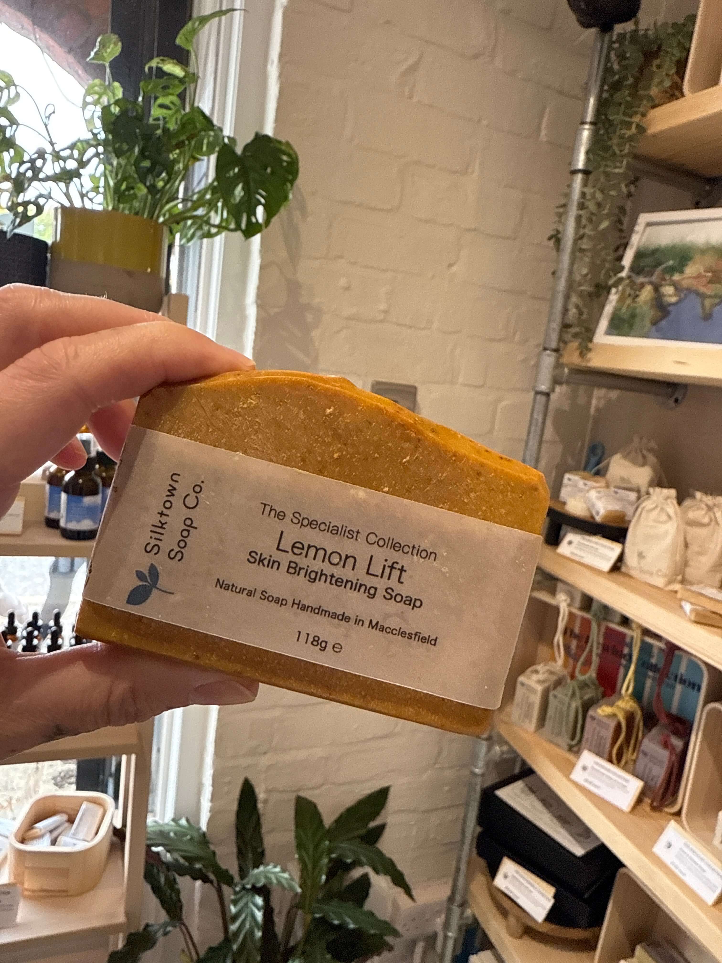 lemon Lift brightening natural soap with kojic acid held in the air with shop in background.