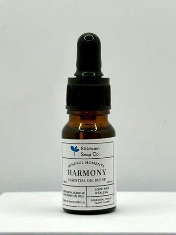 A small dropper bottle of Natural Essential Oil Harmony Blend with labels indicating the key ingredients such as Geranium, Pine, and Ylang-Ylang, and the brand Silly Billy.