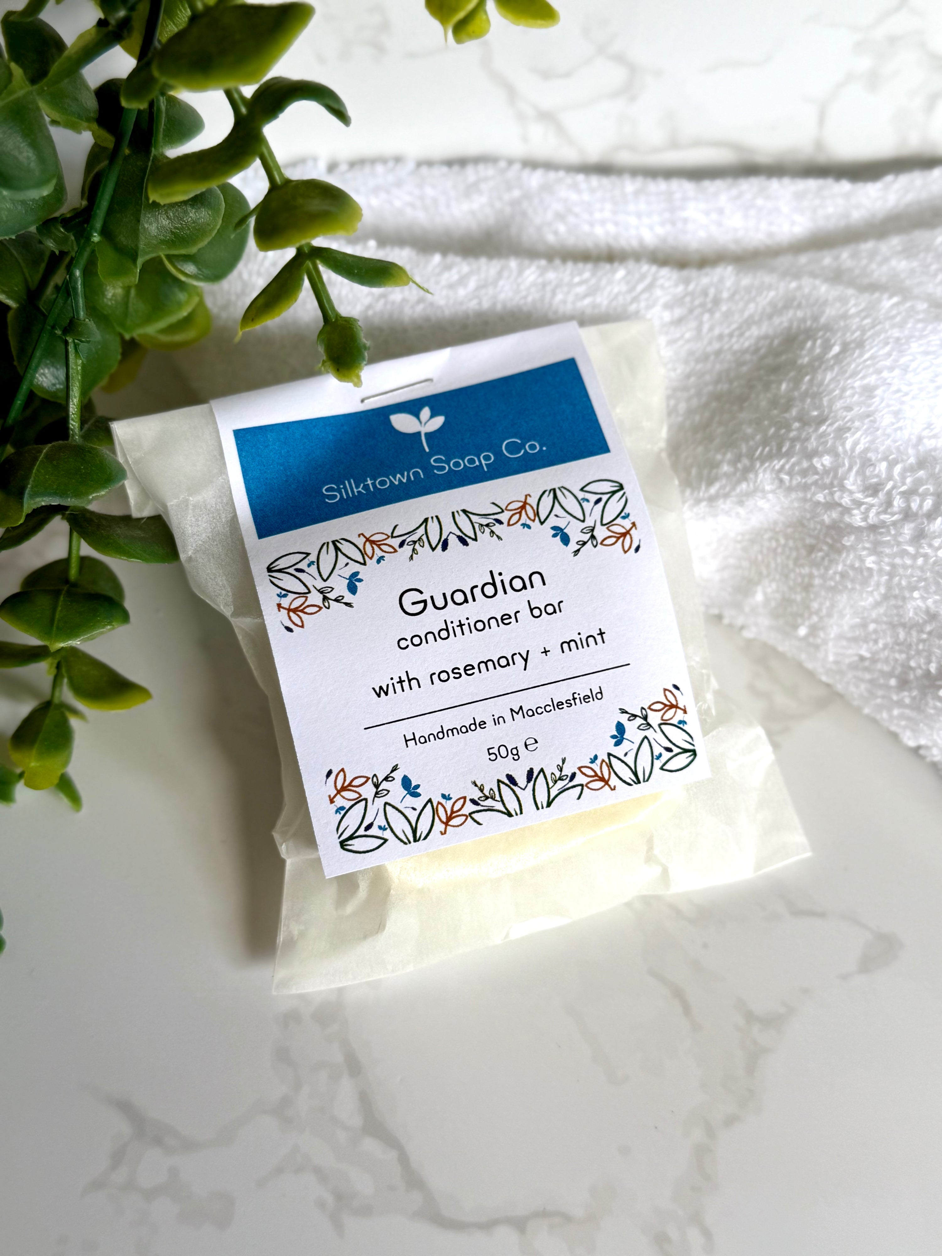 Packaged Rosemary &amp; Peppermint Natural Conditioner Bar on a marble dish with a towel and foliage