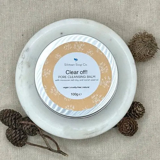 A large tin of vegan friendly Pore cleansing facial balm on a dish surrounded by fir cones