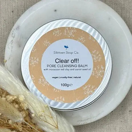 A large tin of vegan friendly Pore cleansing facial balm on a dish next to dried flowers and a towel
